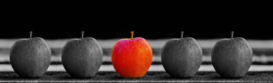 One red apple surrounded by black and white apples